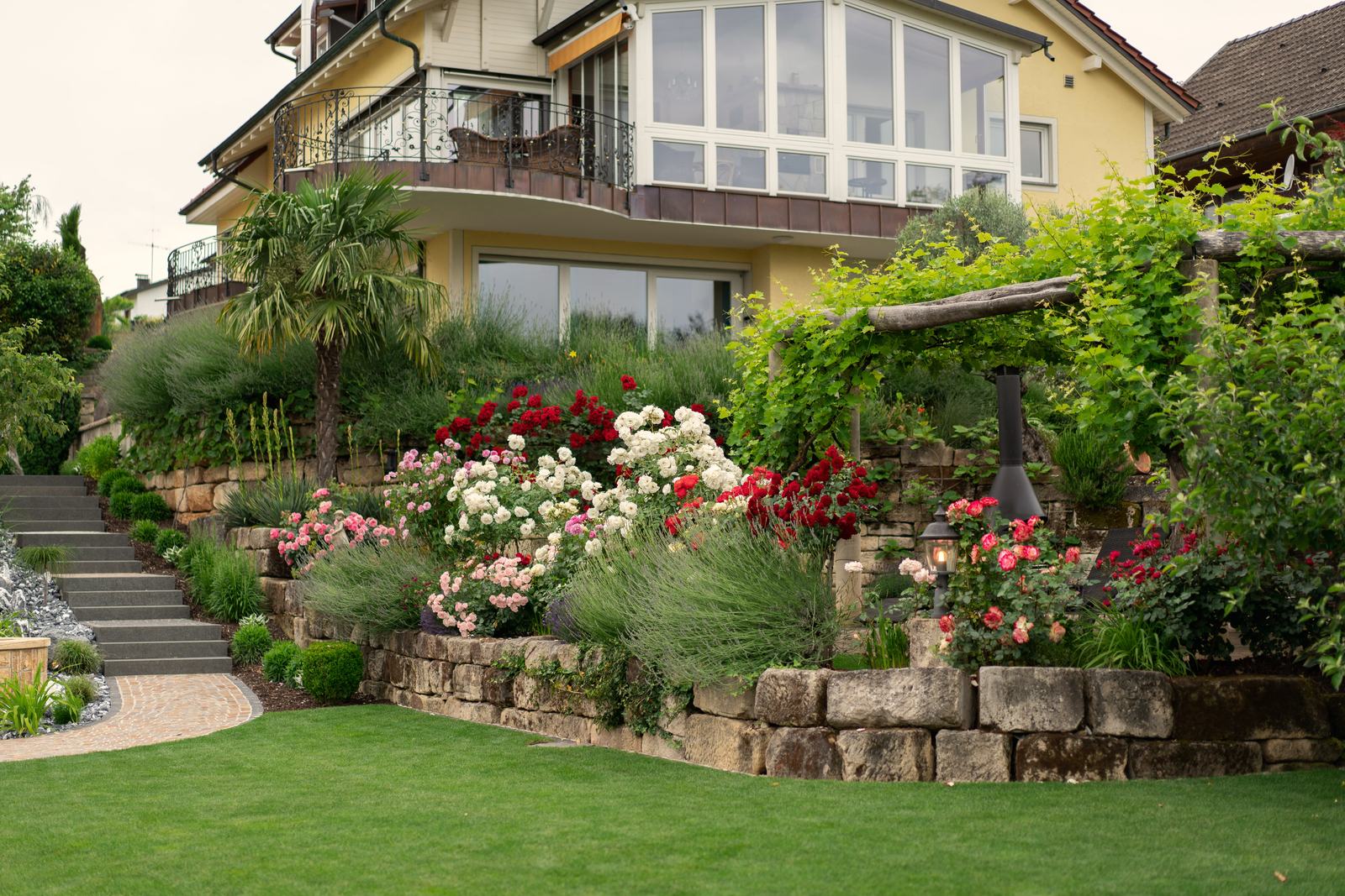 Gartenbereich mit Rosenbeet, Palme und Natursteinmauer