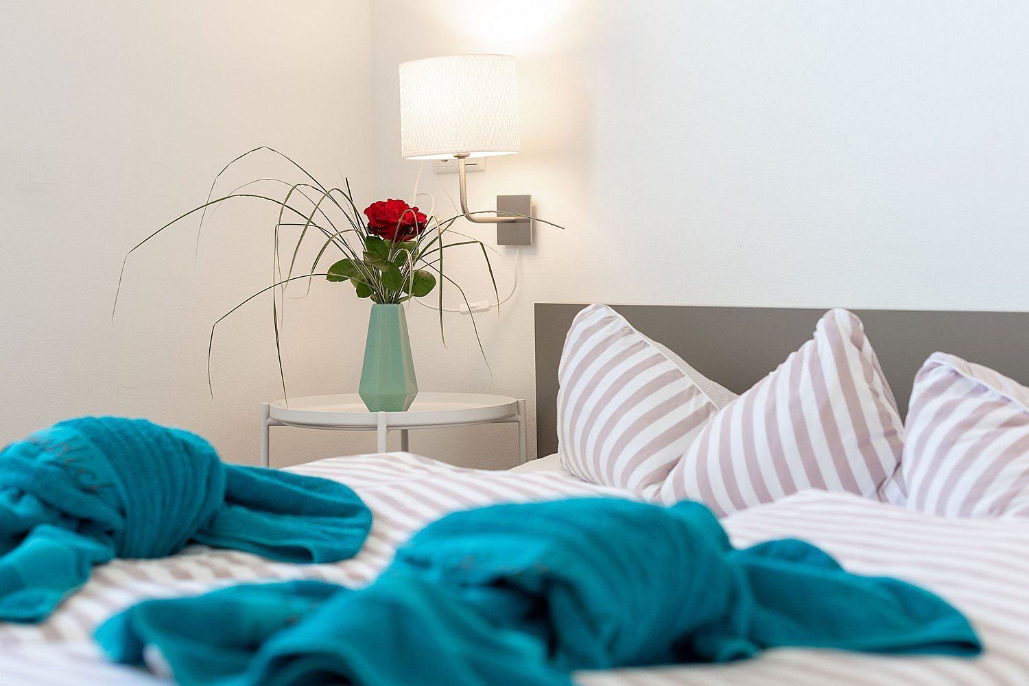Gemütliches Bett-Detail mit Rose und Nachttischlampe